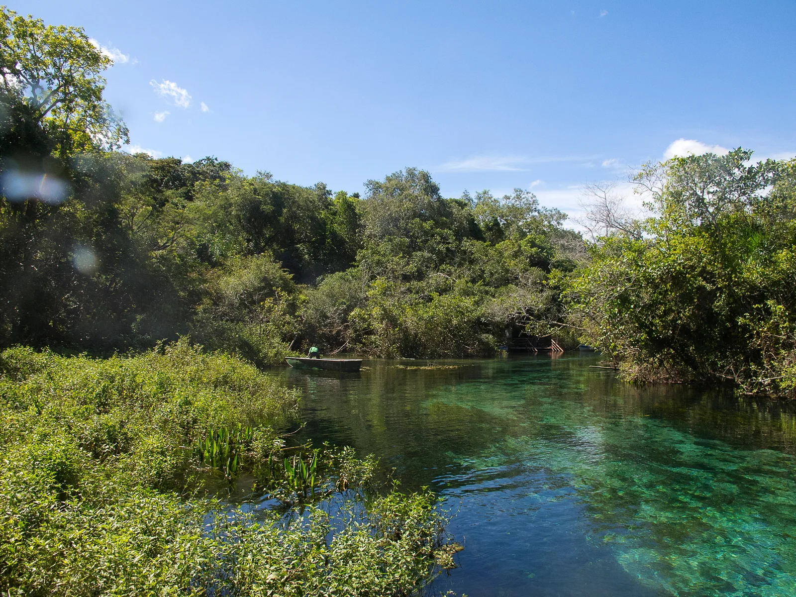 A clear turquoise spring-fed river in Bonito with forest on both banks and a wooden boat moored at the far end