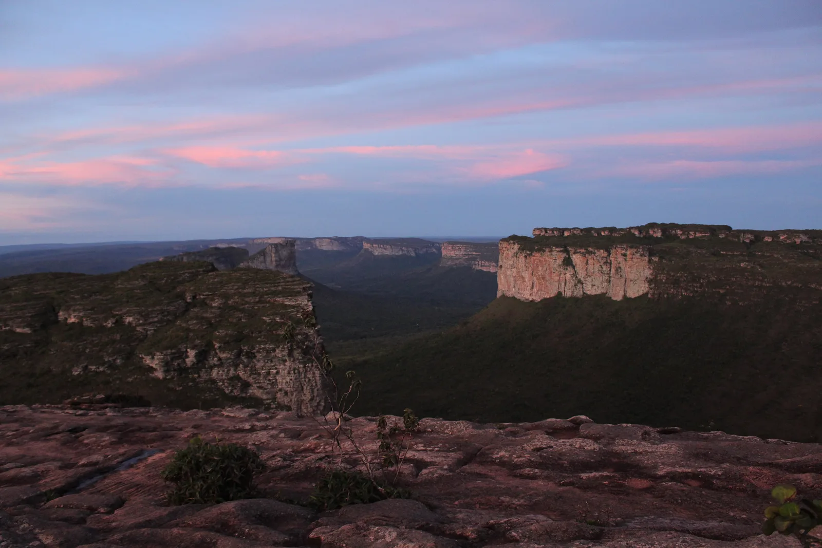 Flat-topped mountains of the Chapada Diamantina at dusk, seen from a rocky ledge with pink cloud above