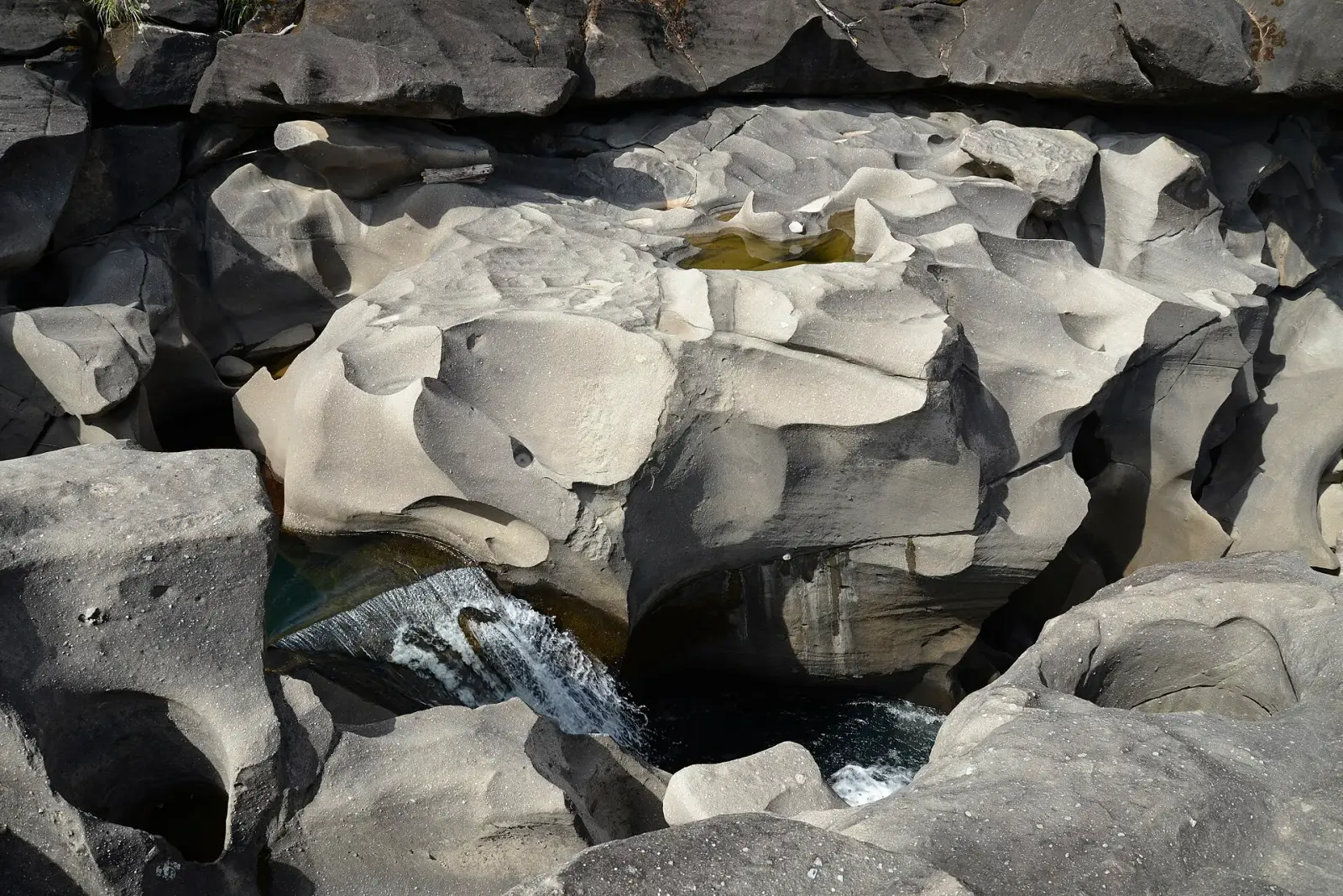 Pale rock sculpted into smooth bowls by the São Miguel river at Vale da Lua