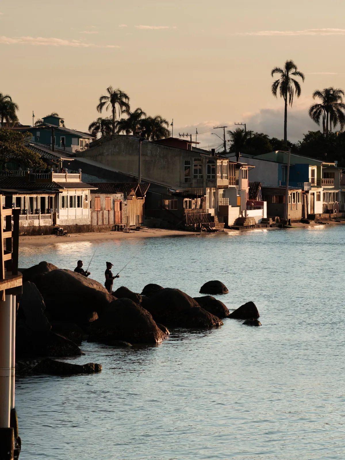 Fishermen on the rocks at golden hour below the Azorean waterfront houses of Florianópolis