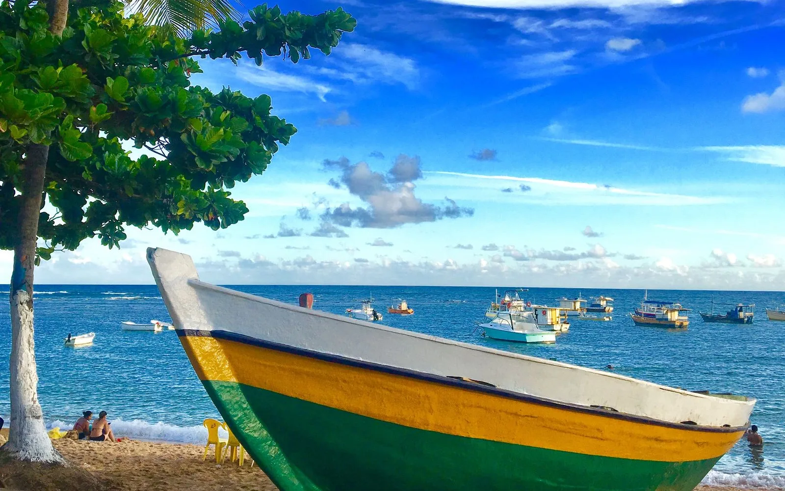 A wooden fishing boat on the sand at Praia do Forte, with boats anchored offshore