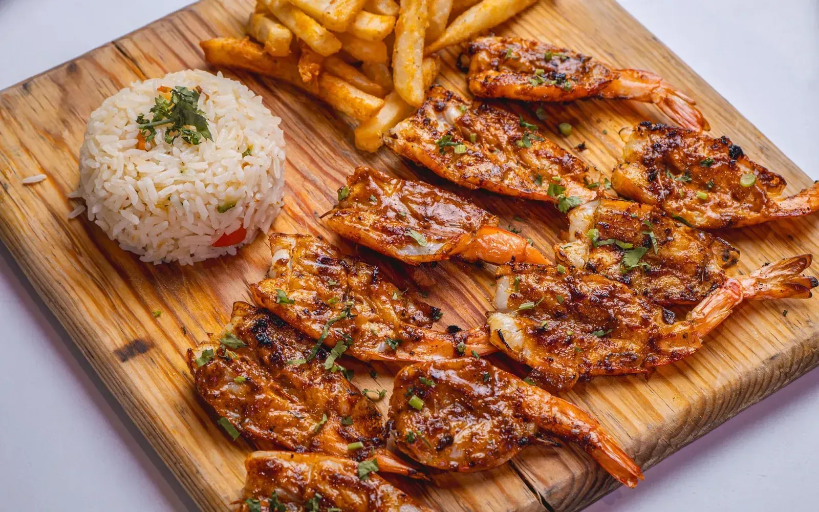 Grilled prawns served with rice and chips on a rustic wooden board