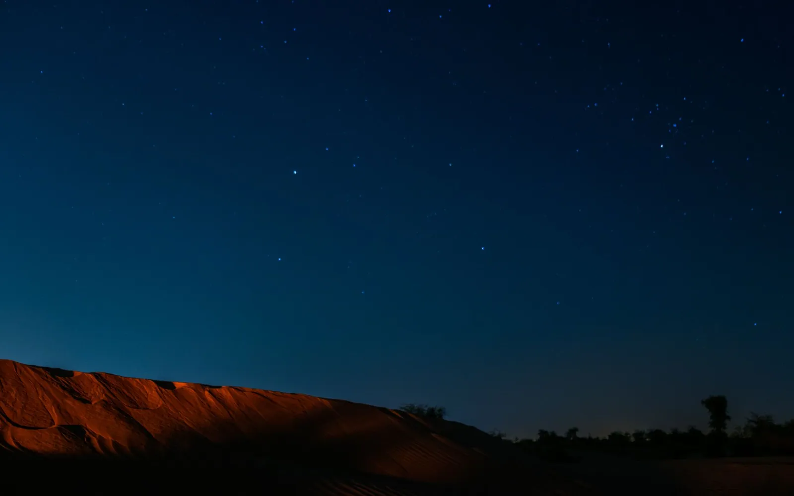 A dark dune ridge under a deep blue sky thick with stars