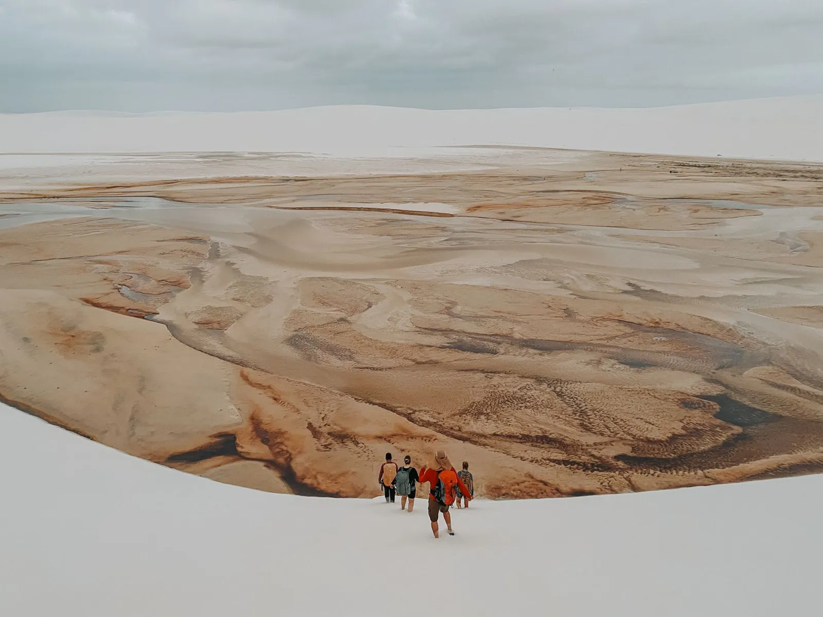 A small group of trekkers strung out across a vast expanse of pale dunes