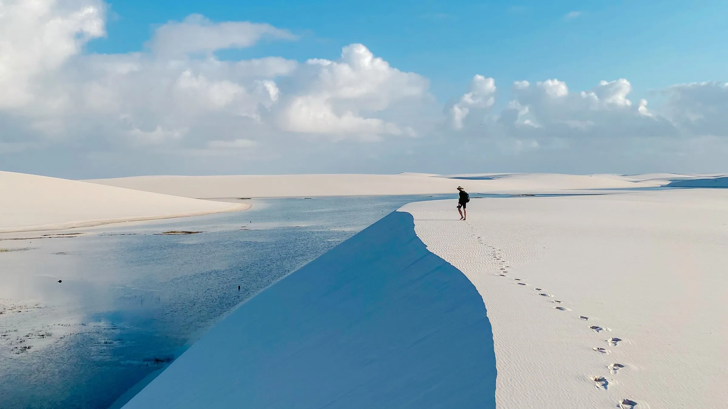 A single line of trekkers on a white dune crest at dawn, lagoons stretching to the horizon