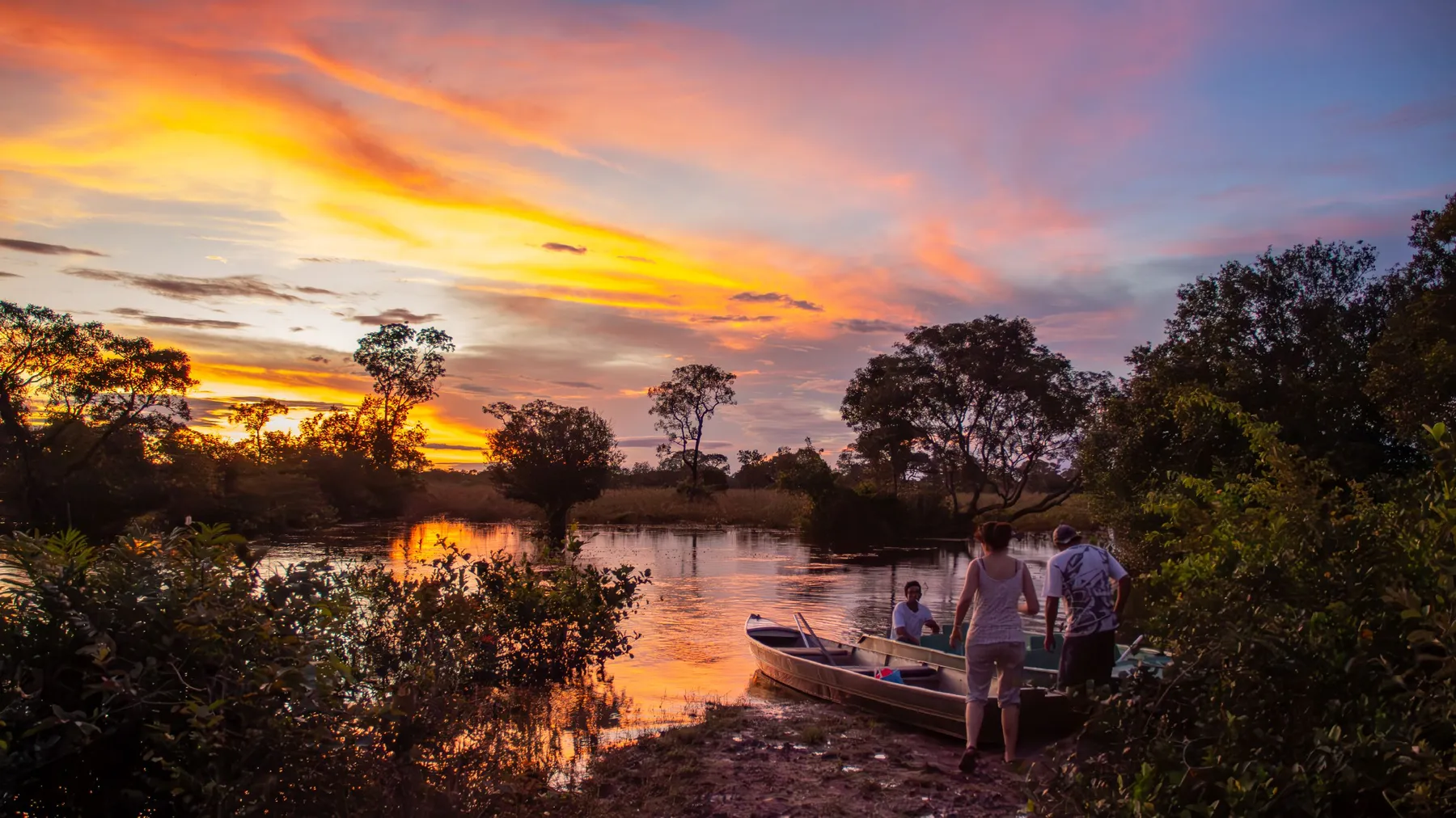 Travelers walking down to a small boat under a blazing Pantanal sunset