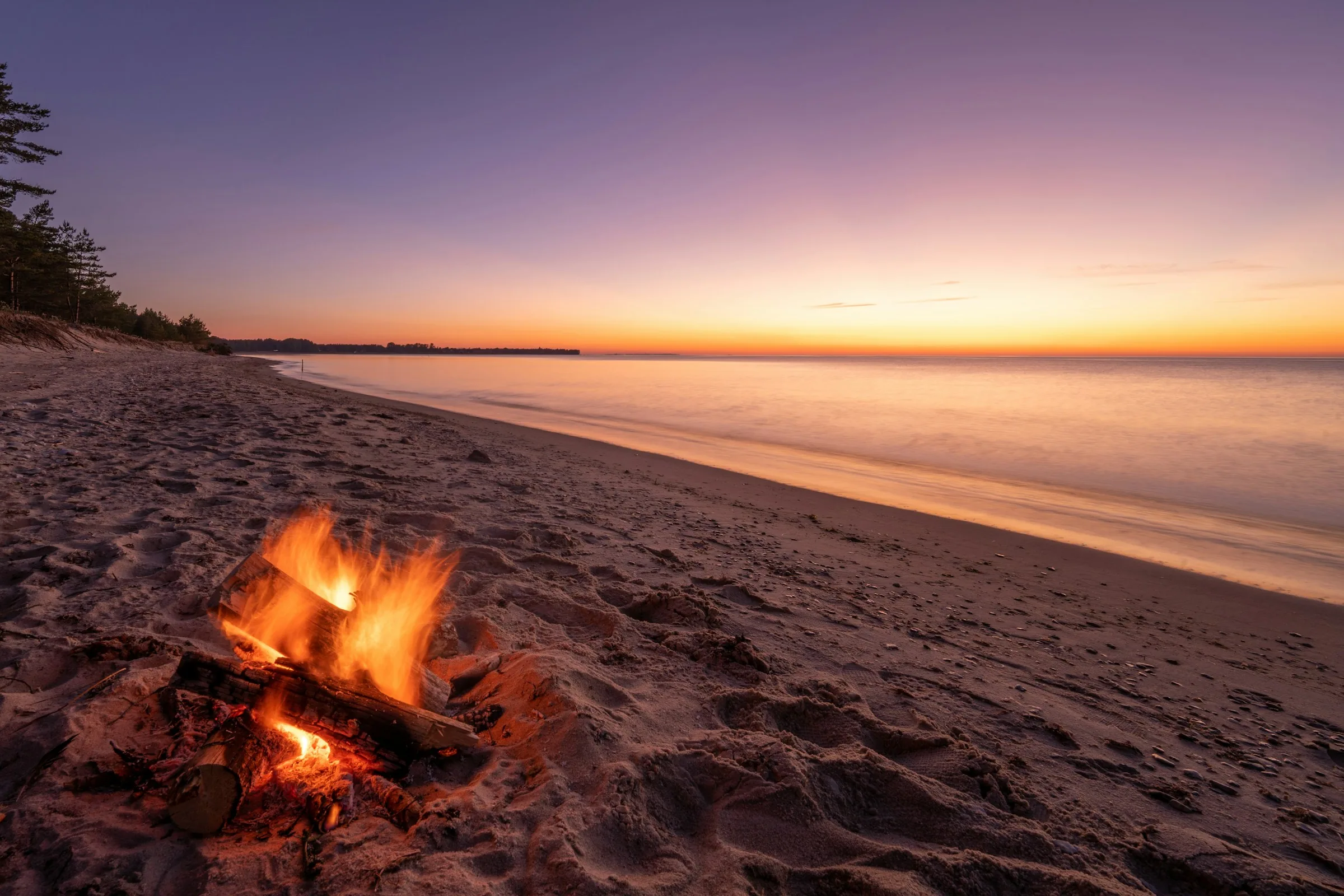 A fire burning on an empty beach at sunset