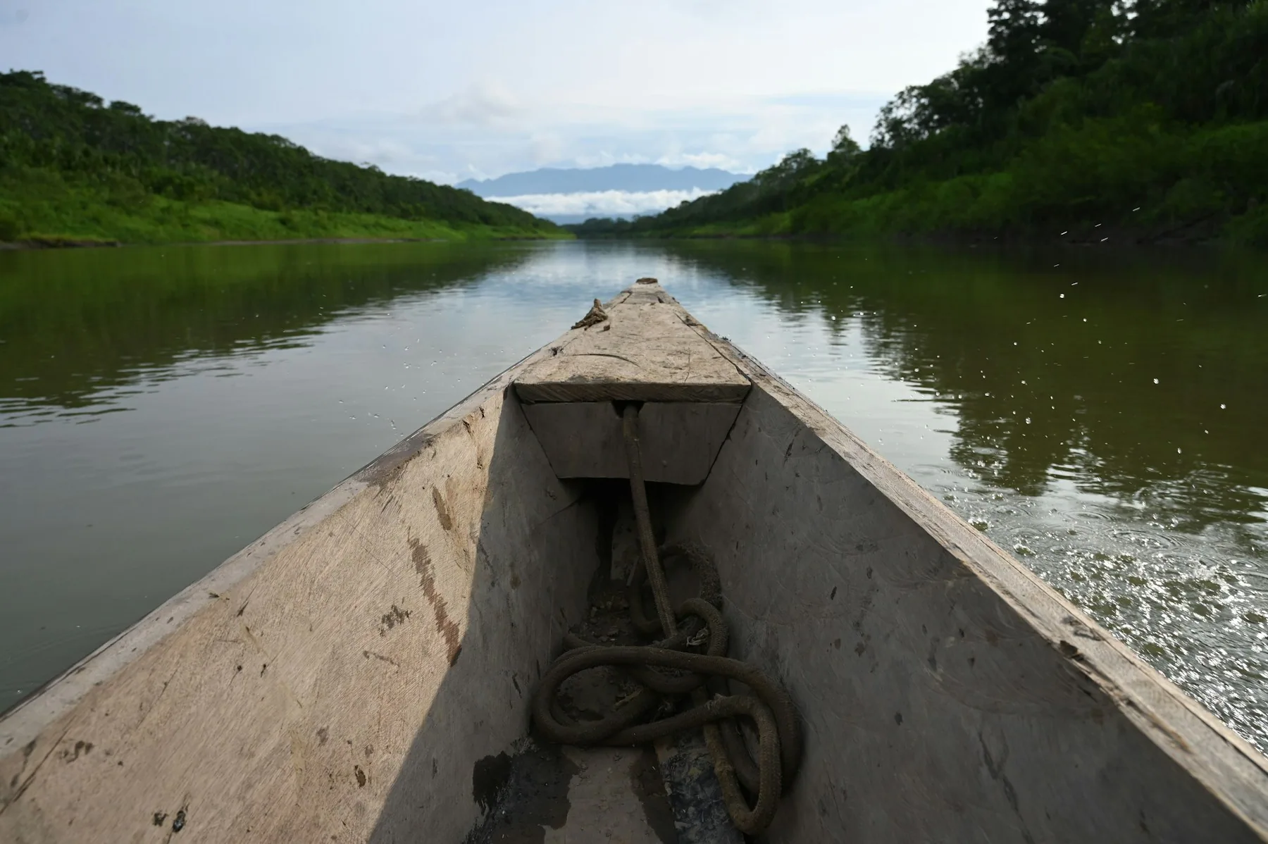 A wooden canoe on a calm river below forested banks
