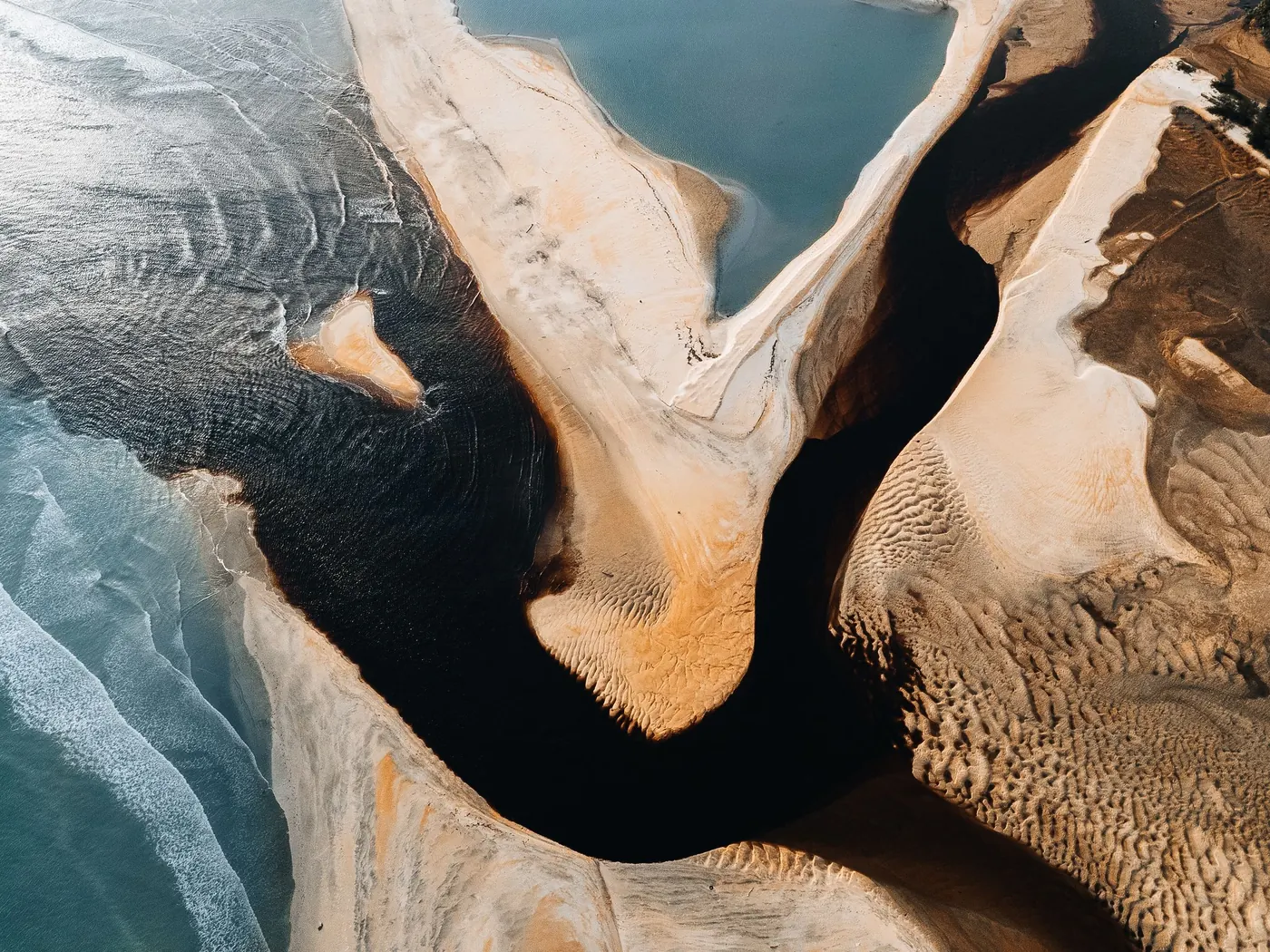 An aerial of pale sandbanks braiding through dark tidal channels where river meets sea