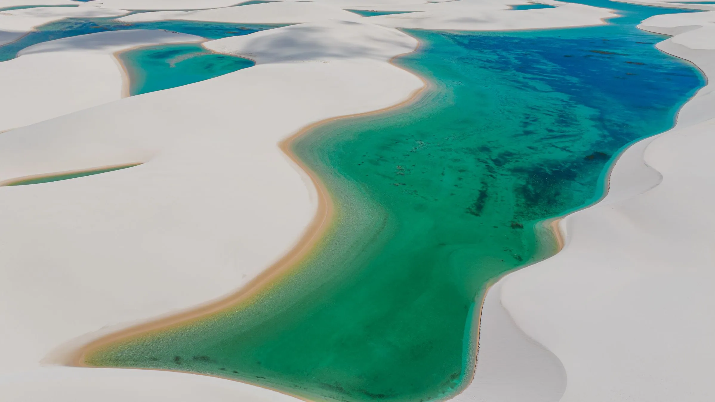 Turquoise rainwater lagoons winding between white dunes to the horizon