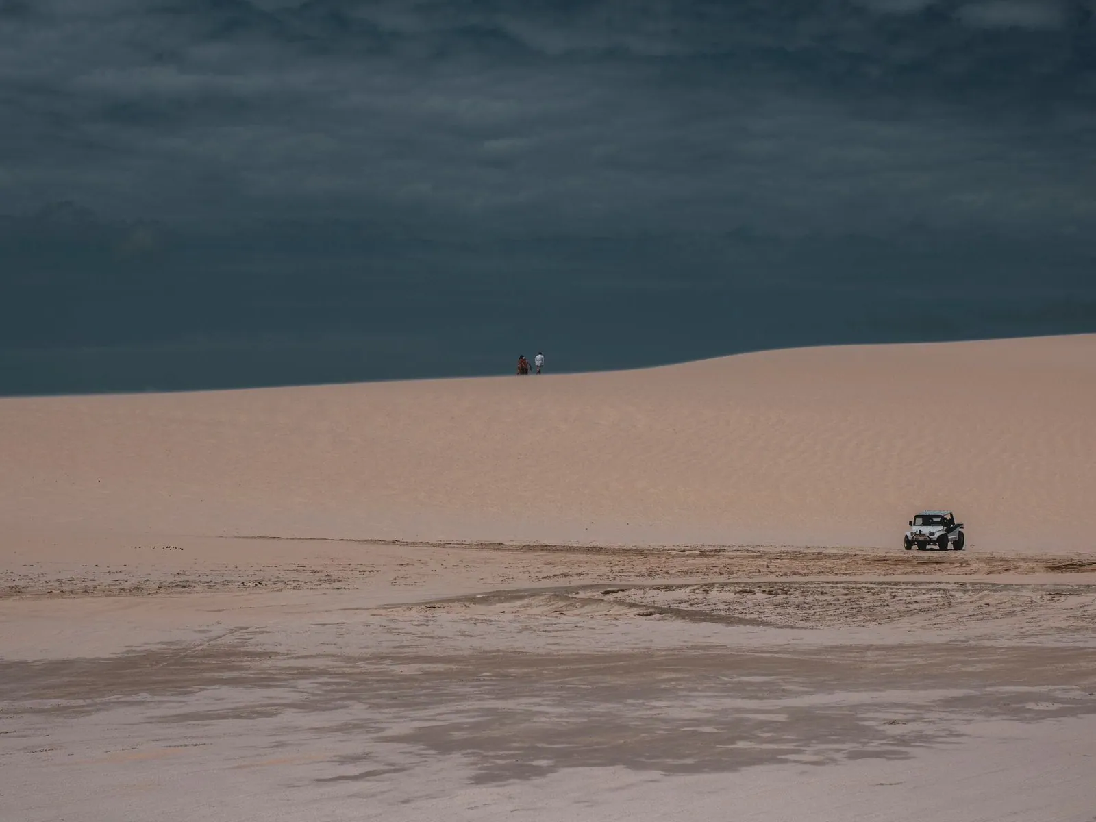 A 4x4 running along a vast empty beach with dunes rising inland