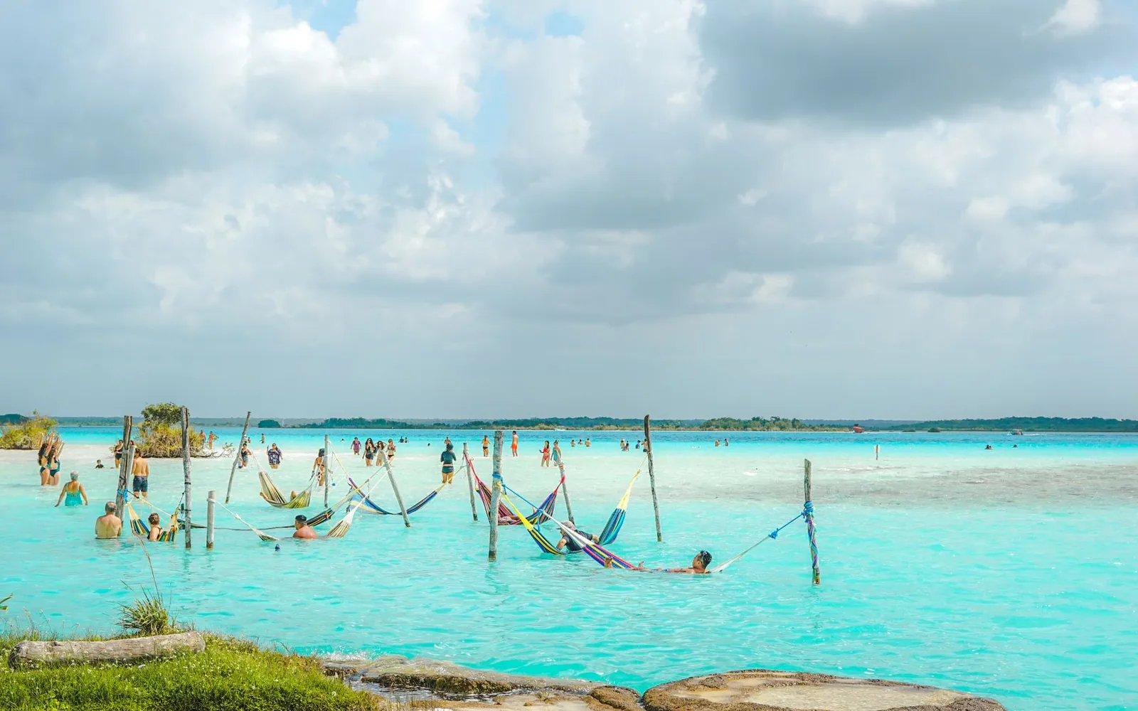A row of hammocks strung over the shallow turquoise water of Lagoa do Paraíso