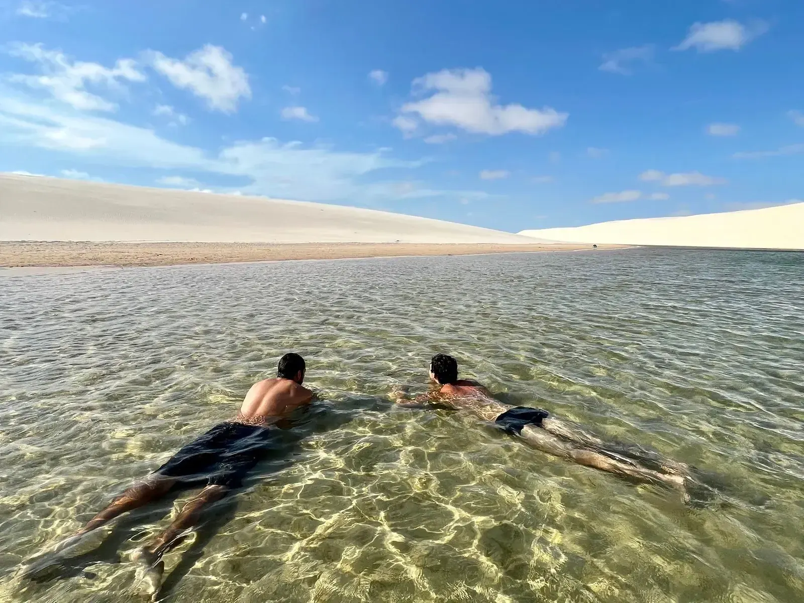 Swimmers floating in a turquoise lagoon cupped between steep white dunes