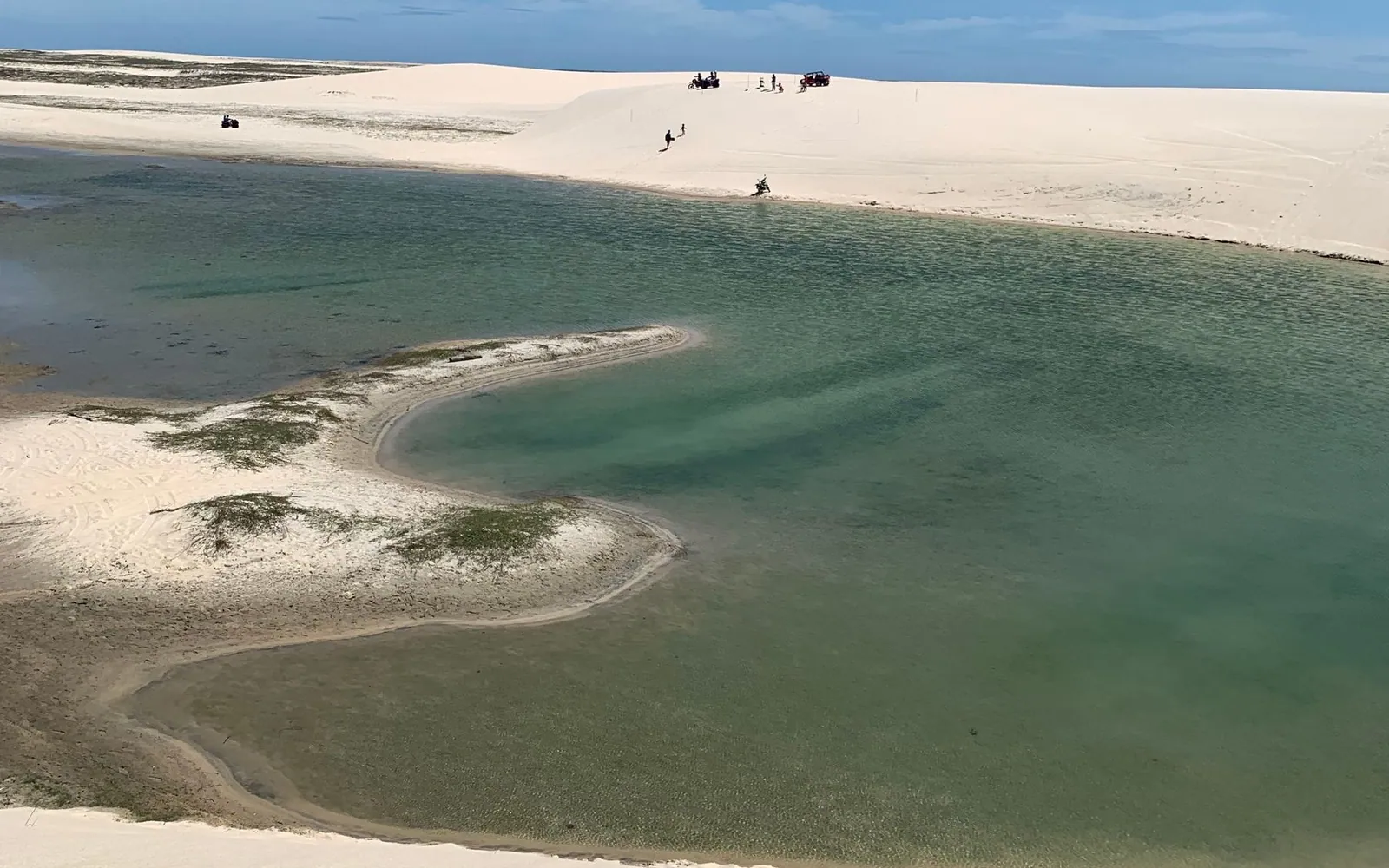 A calm lagoon lying between smooth pale dunes under a clear sky