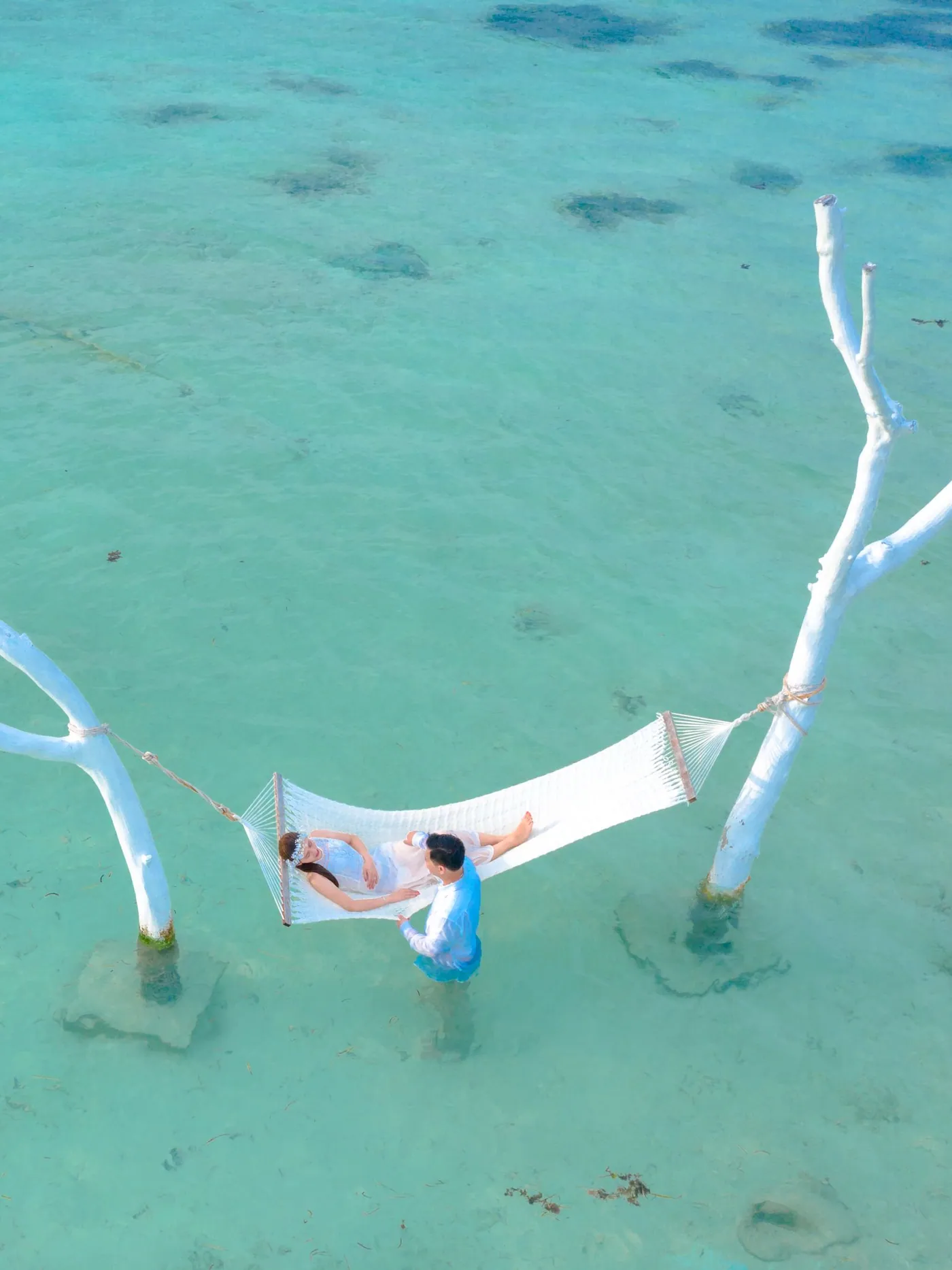 A hammock slung over shallow turquoise water, seen from directly above