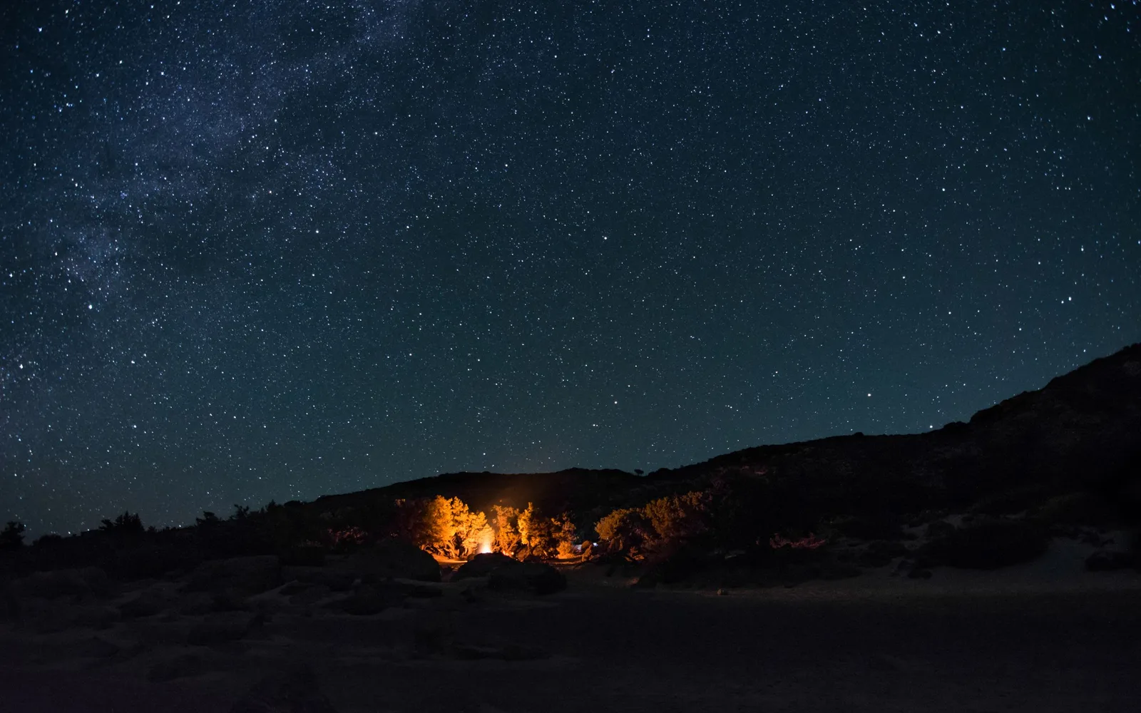 A fire burning in open country under a sky thick with stars