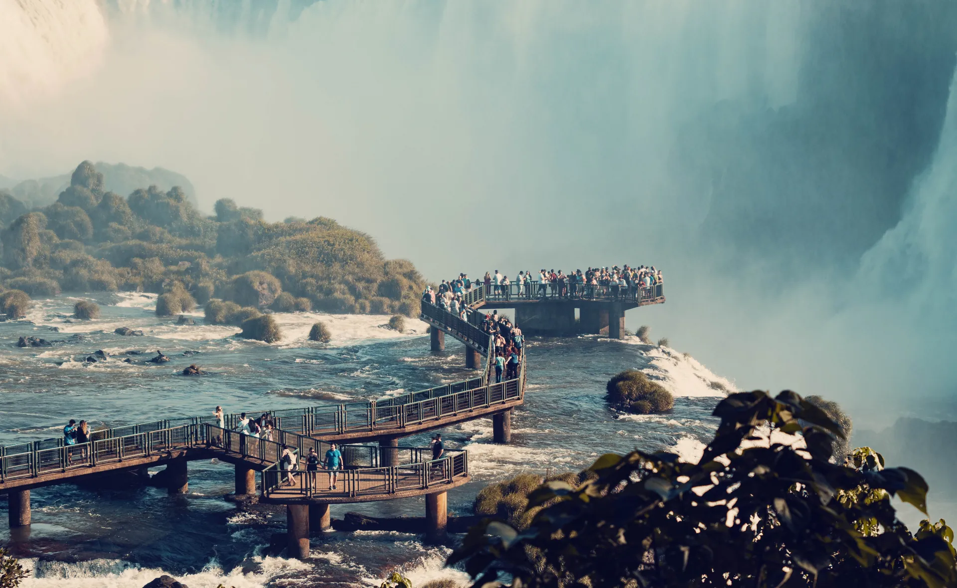 A coati on a walkway at Iguaçu with a rainbow over the falls behind
