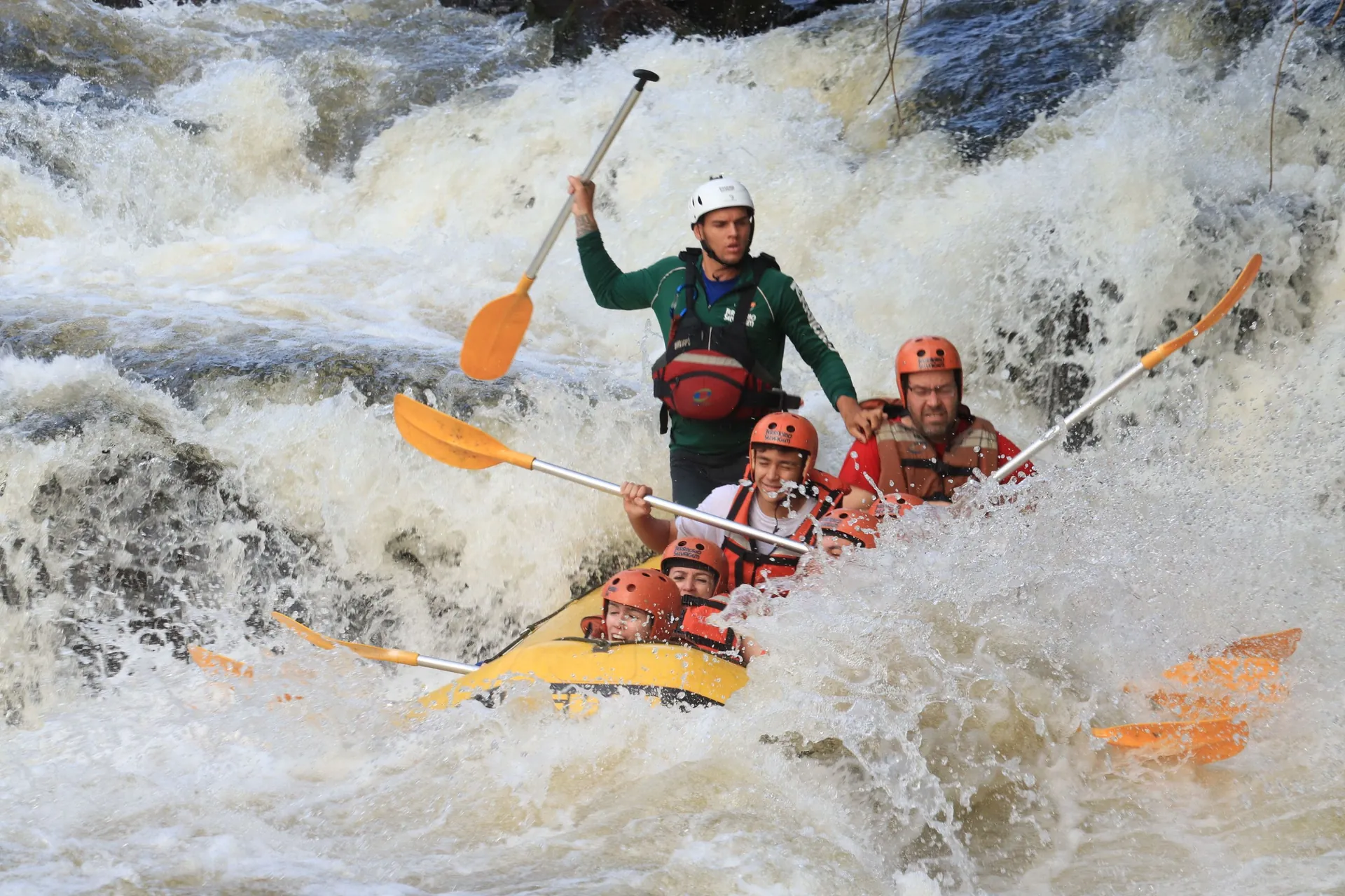 An inflatable boat full of drenched, laughing passengers driving under the Iguaçu cascades