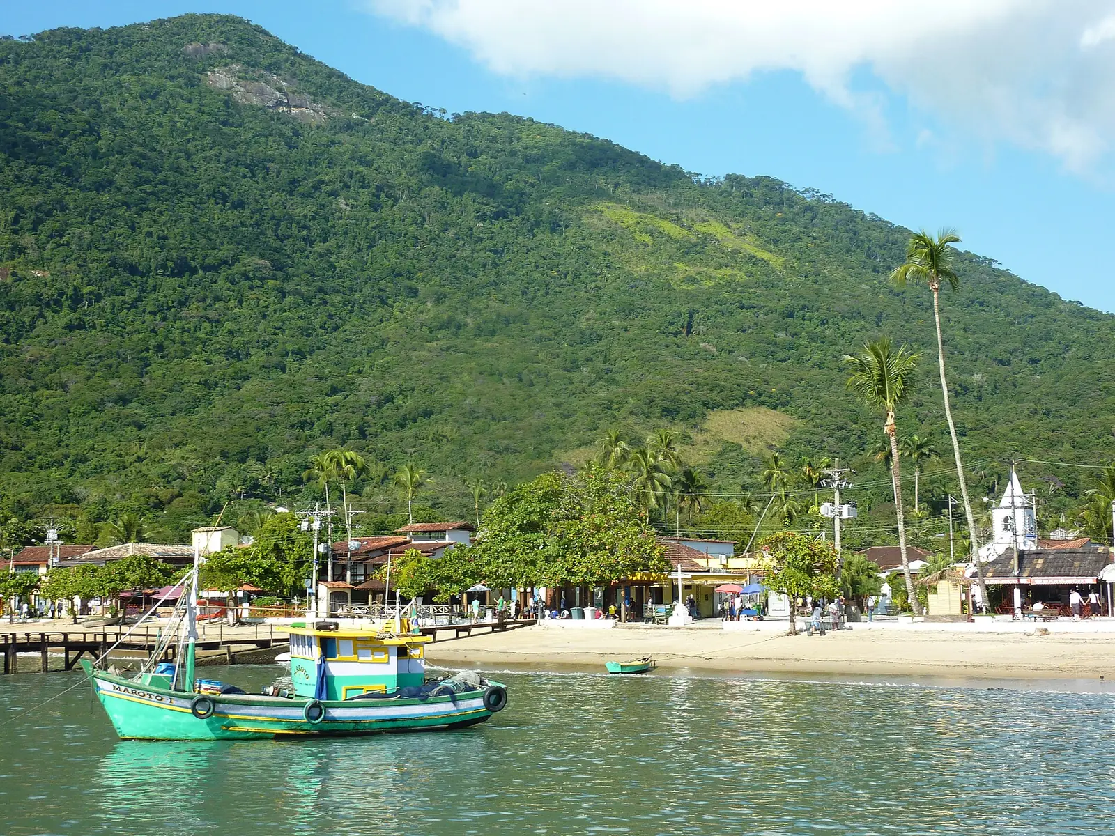 A fishing boat in front of the beach, palms and church of Vila do Abraão on Ilha Grande