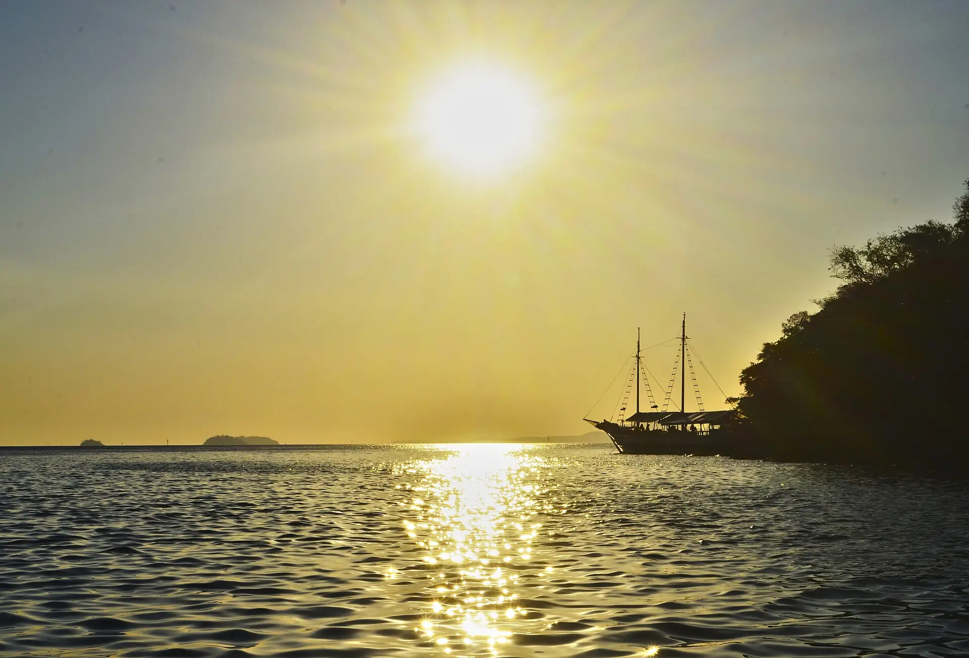 A schooner silhouetted against a golden sunset in a calm Ilha Grande bay