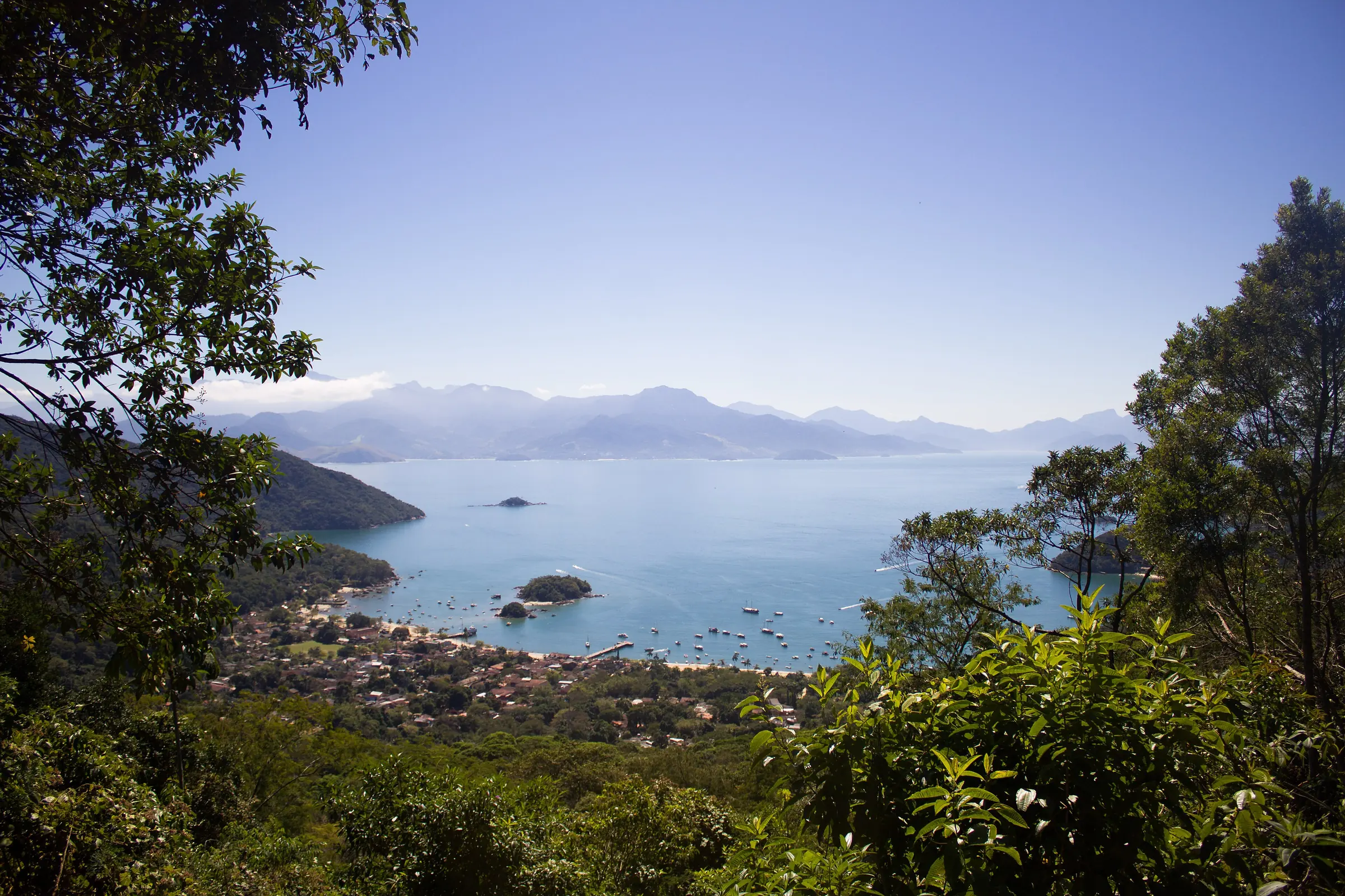 View through the rainforest over the bay of Vila do Abraão on Ilha Grande, with boats at anchor and mountains behind
