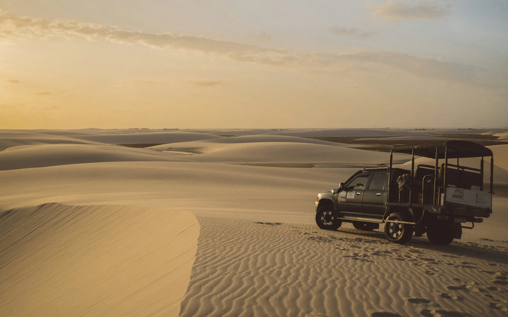 An open-topped 4x4 Toyota truck crossing the dunes toward a lagoon in the Lençóis