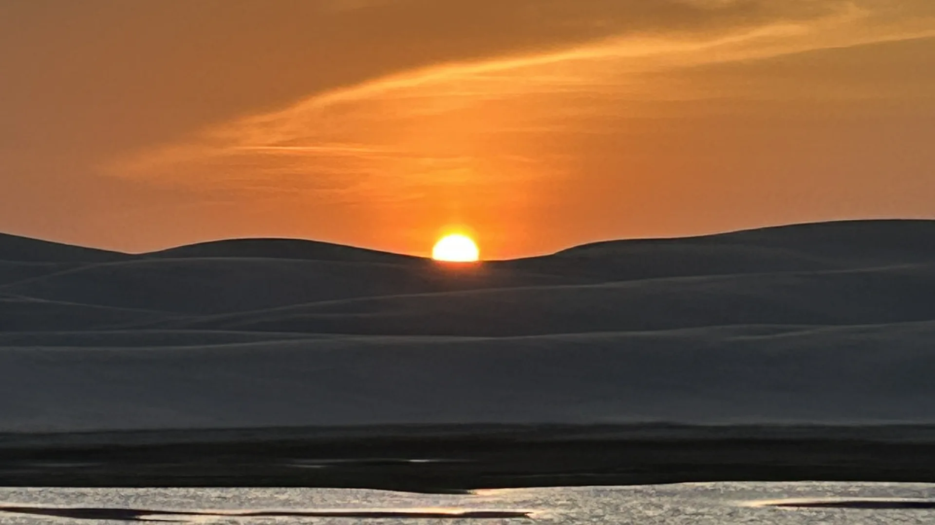 White dunes and a lagoon glowing under a warm sunset in the Lençóis Maranhenses