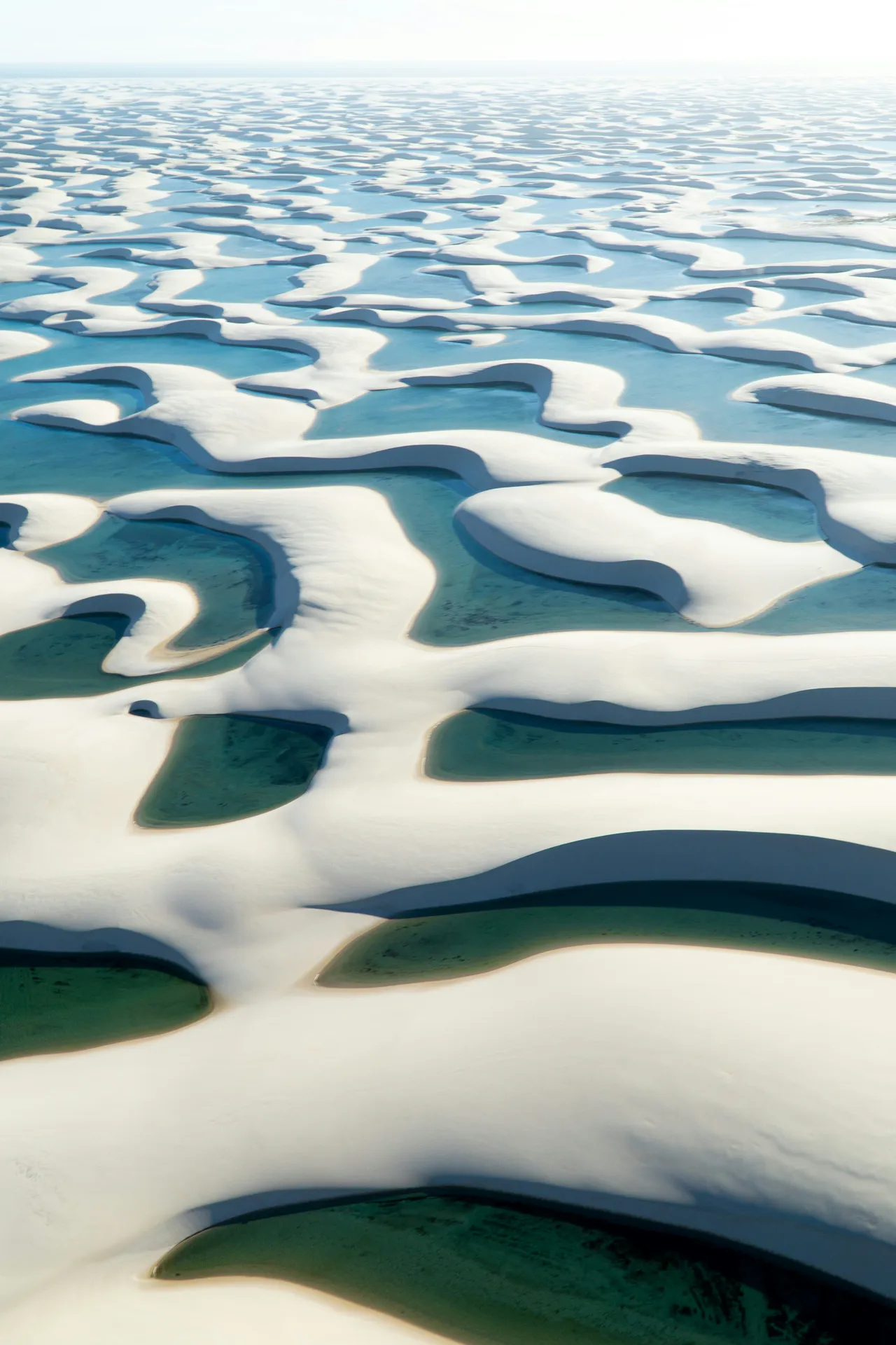 Aerial pattern of white dune ridges and blue lagoons like folded bedsheets