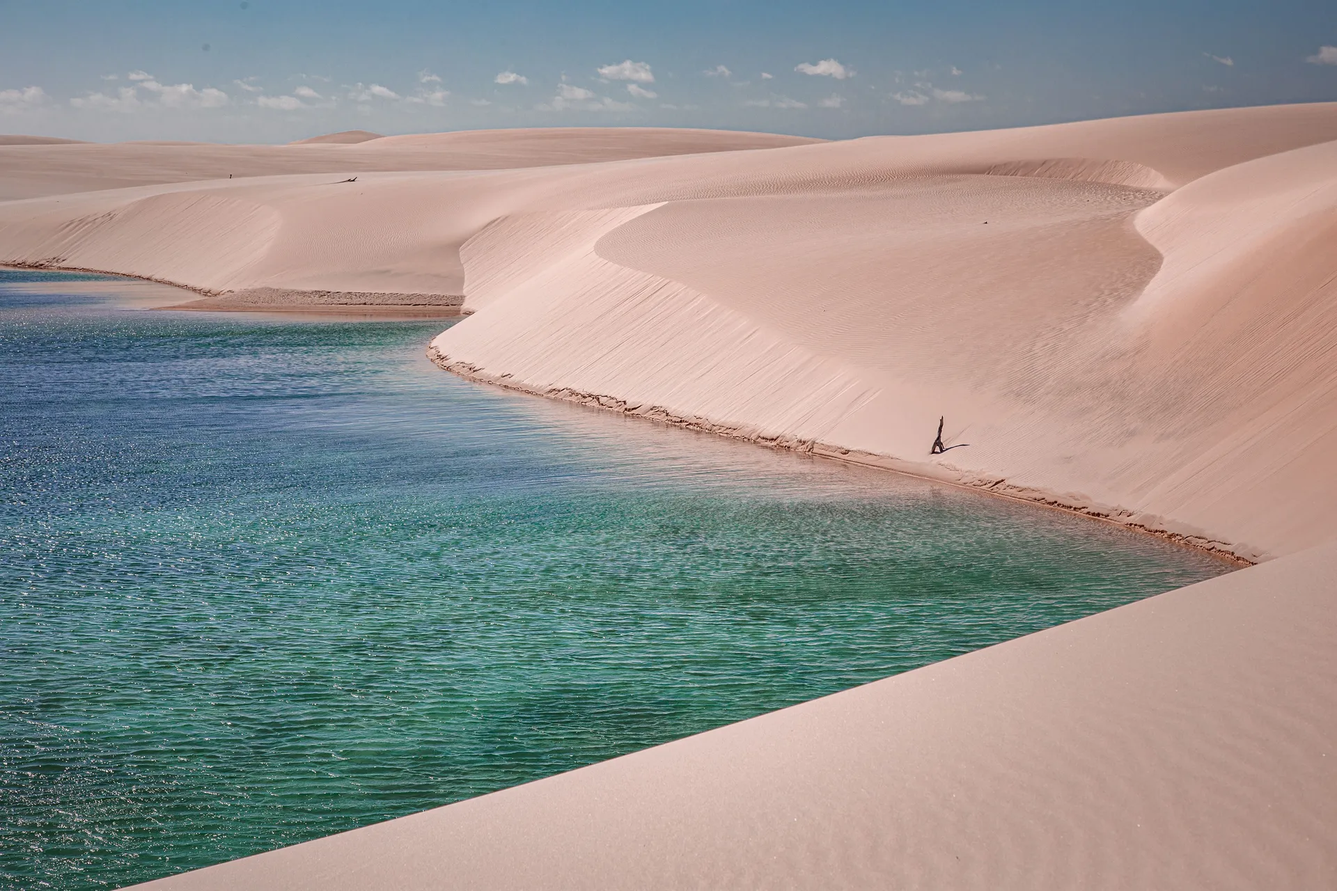 A person standing at the edge of a turquoise lagoon between white sand dunes