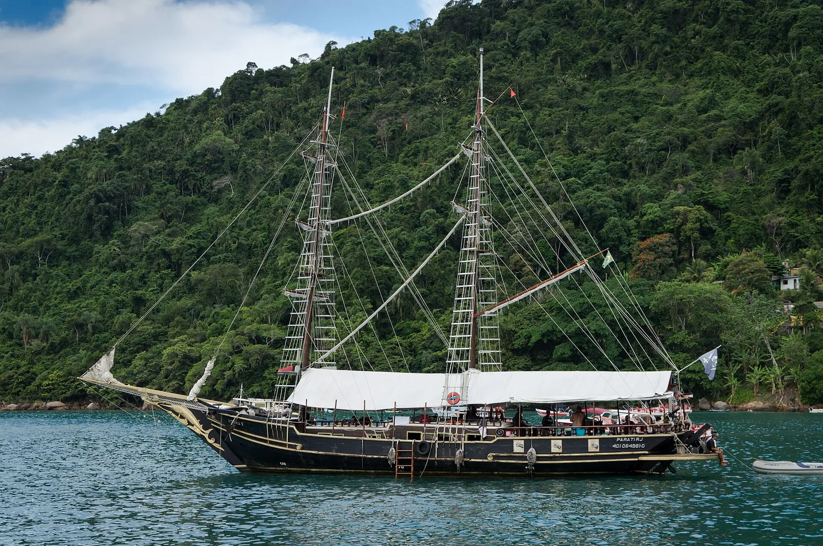 A traditional wooden schooner anchored in the calm, clear waters of Paraty bay