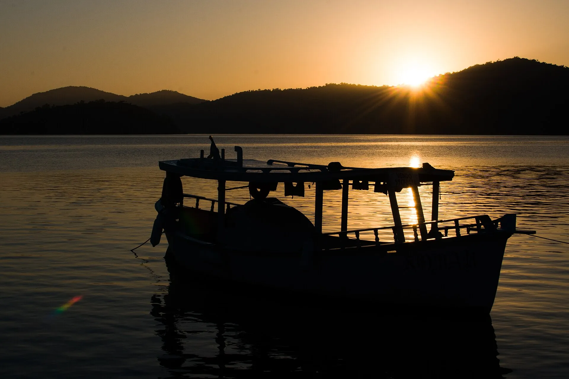 Boats on the calm water of Paraty bay at sunset, the mountains silhouetted behind
