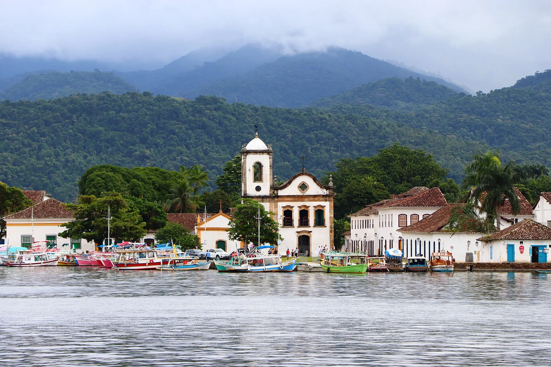The whitewashed Santa Rita church on the Paraty waterfront with colourful fishing boats and forested mountains behind