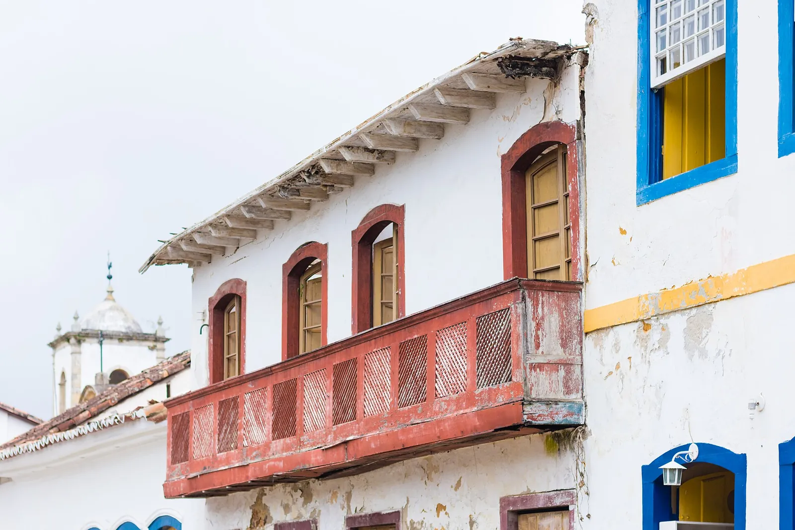 A colonial house in Paraty with a red wooden balcony, blue-framed windows and the white church tower behind