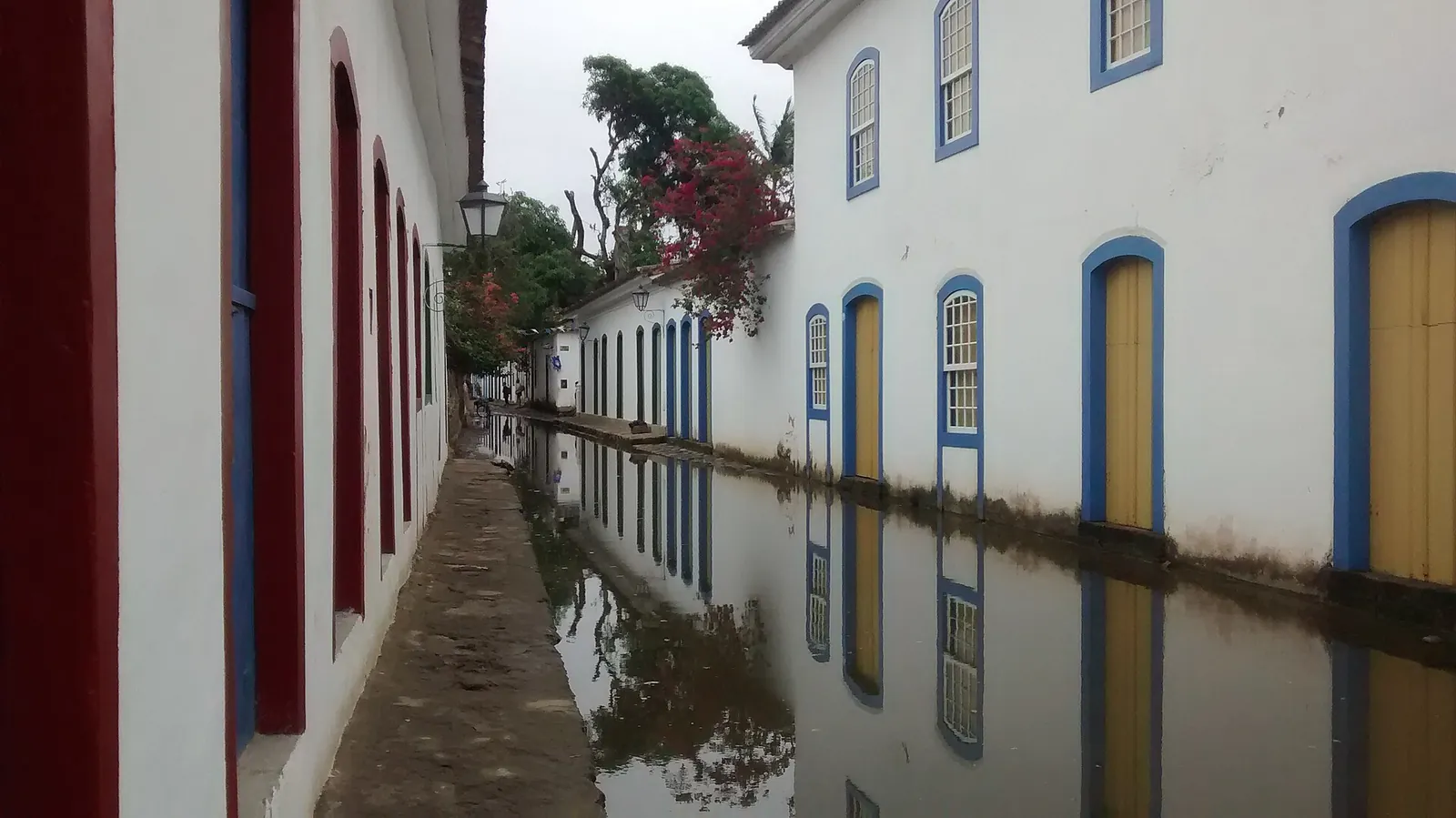A Paraty cobblestone street flooded by the spring tide, colonial facades mirrored in the water