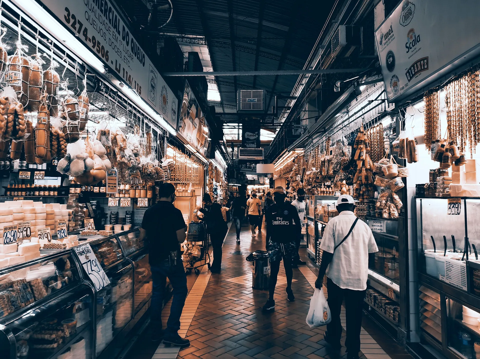 A busy aisle of hanging cured meats, cheeses and stalls inside São Paulo’s Mercado Municipal